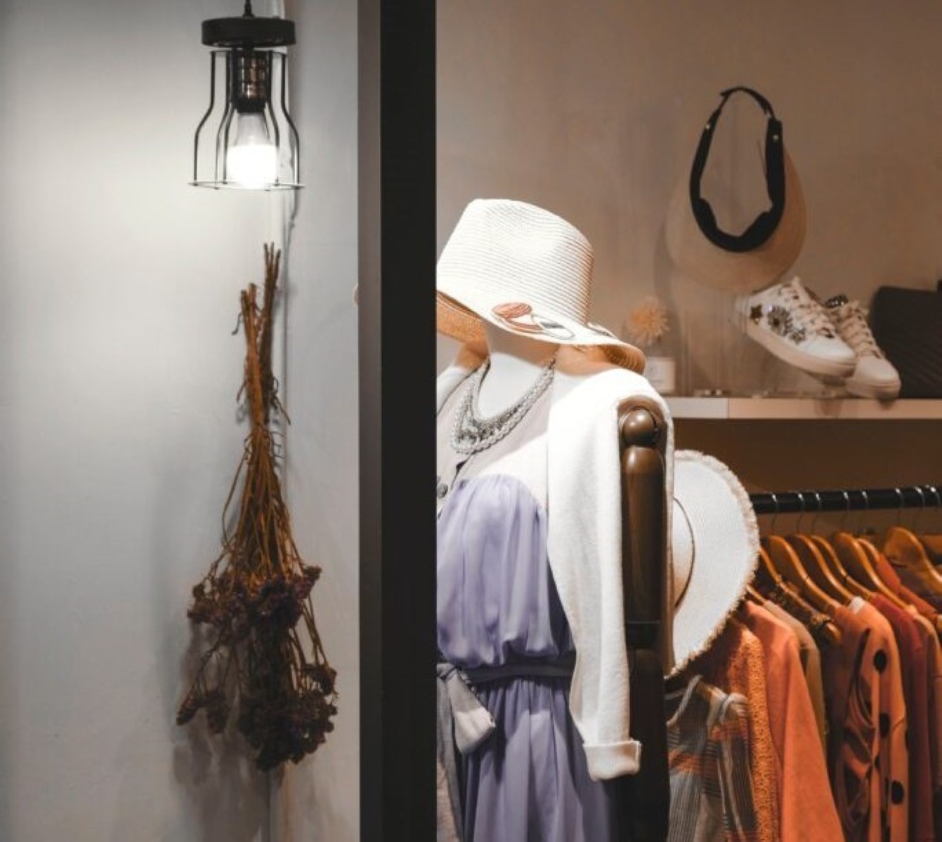 Mannequin in a boutique in Larnaca, Cyprus, wearing a lavender dress and wide-brimmed hat, with assorted clothing in the background and dried botanicals on the side.