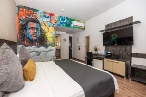 Boutique hotel room in Larnaca with colorful portrait mural, double bed, TV and modern desk area