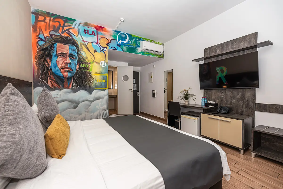 Boutique hotel room in Larnaca with colorful portrait mural, double bed, TV and modern desk area